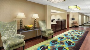 Eine Hotellobby mit einer Rezeption, zwei Sesseln, einem kleinen Tisch mit Obstschale und einem gemusterten Teppich.