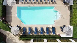 Luftaufnahme eines Poolbereichs mit Liegestühlen und Sonnenschirmen, umgeben von viel Grün.