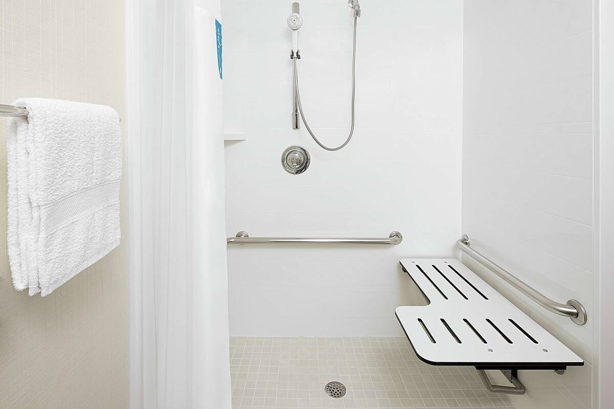 A bathroom with a white shower, a grab bar, and a white towel on a rack.