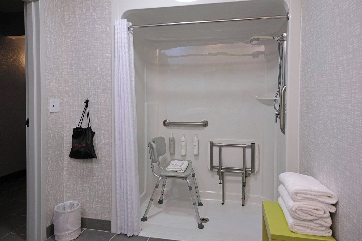 Un baño pequeño y privado con espacio para silla de ruedas, barra de apoyo y una pila de toallas.