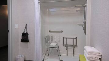 Un baño pequeño y privado con espacio para silla de ruedas, barra de apoyo y una pila de toallas.