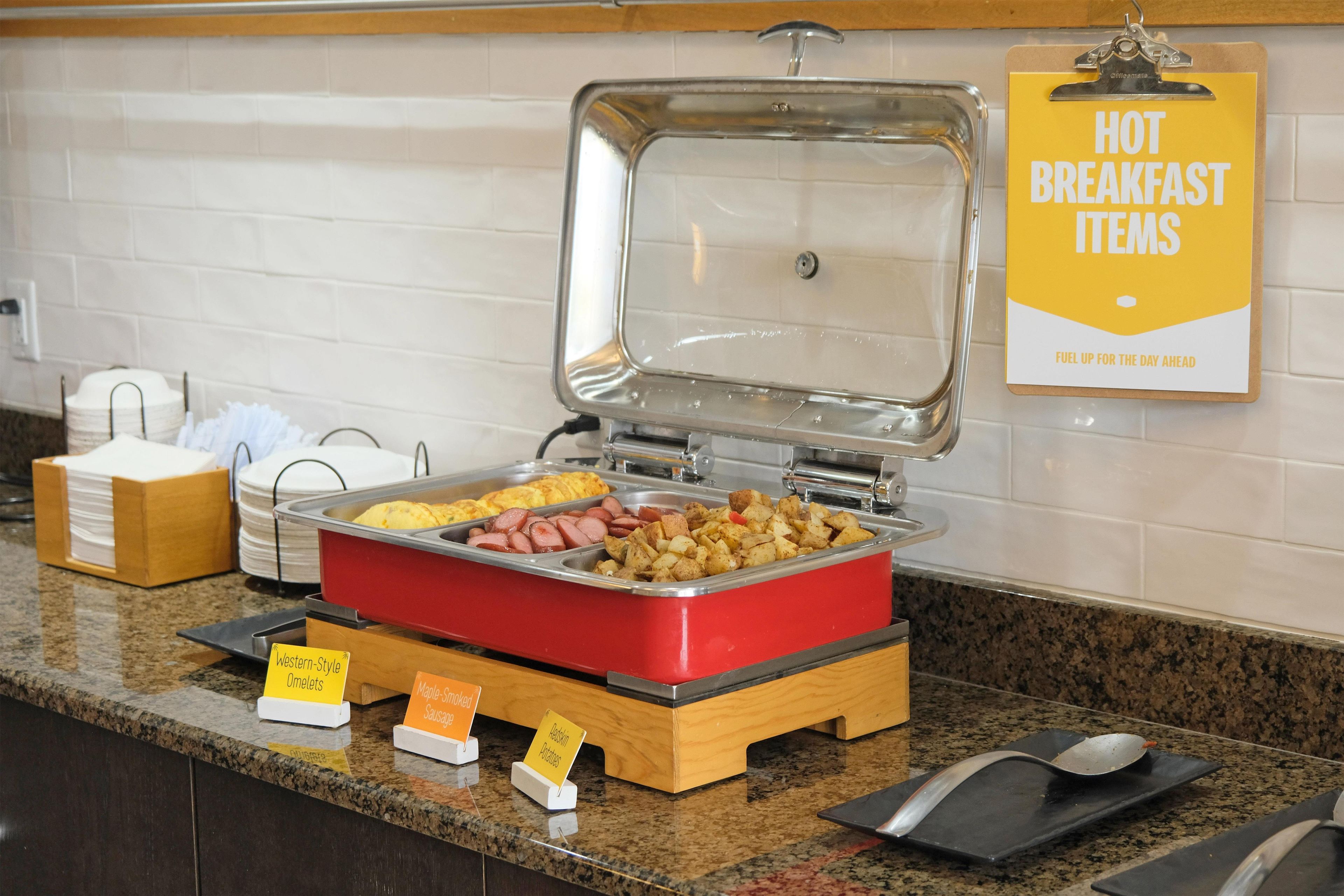 Disposición de buffet con alimentos identificados, como tortillas, salchichas y papas.