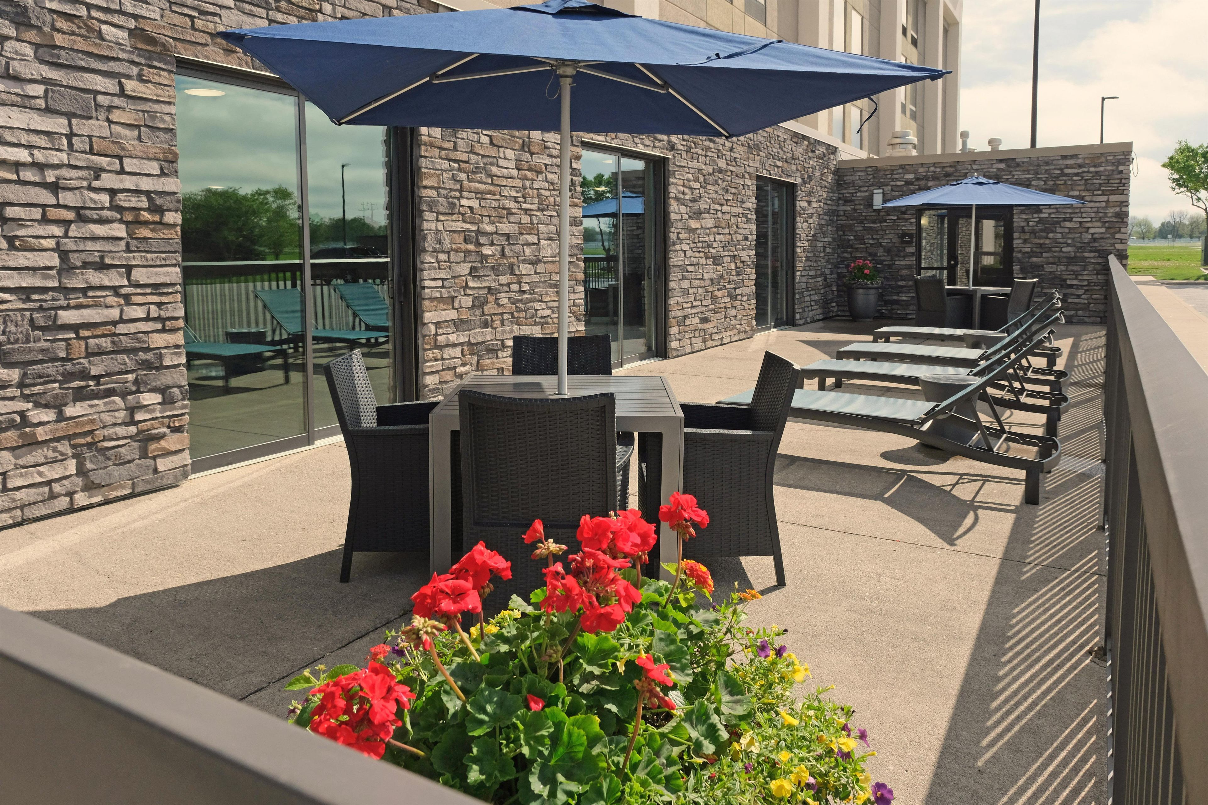 An outdoor patio with stone walls, a table, chairs, and a blue umbrella.