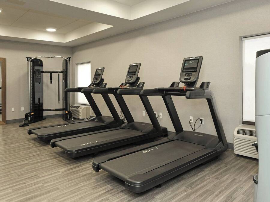 A gym with four treadmills, a mirrored wall, and a large air conditioning unit.