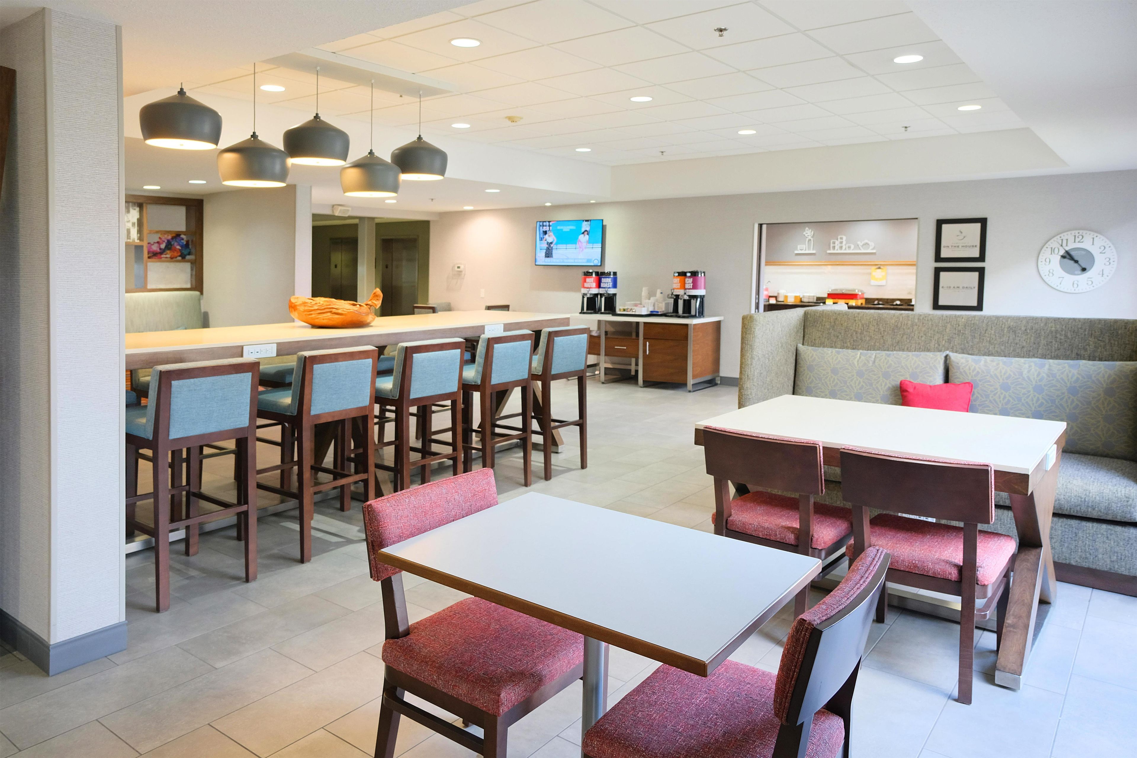 Un espace de restauration moderne dans un hôtel, comprenant une longue table conviviale, des tables individuelles et un coin salon avec un canapé et des fauteuils.