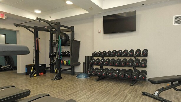 Una sala de gimnàstica equipada amb aparells de musculació, peses, cintes de córrer i una televisió penjada a la paret.