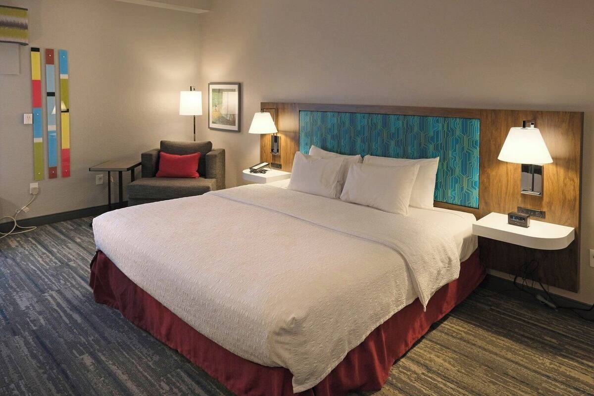 Camera d'albergo con un letto grande, due comodini, una sedia, una scrivania e una parete con decorazioni colorate.