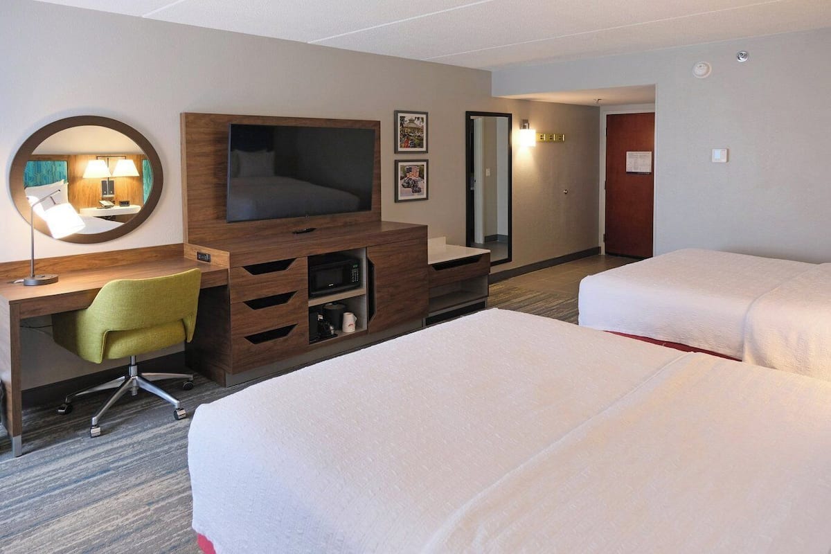 Camera d'albergo con un letto, una scrivania con una sedia, una TV, uno specchio e una porta.