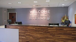 Taulell de recepció amb un cartell que diu 'WELCOME TO THE BUCK EYE STATE', taulell de fusta i un arranjament floral.
