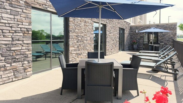 An outdoor patio with stone walls, wicker furniture, and a blue umbrella. - Hampton Inn Lima (Lima)