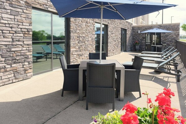 An outdoor patio with stone walls, wicker furniture, and a blue umbrella. - Hampton Inn Lima (Lima)
