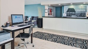 Un'area reception con un computer, una scrivania, una sedia, un tappeto decorato e una parete con un grande poster.