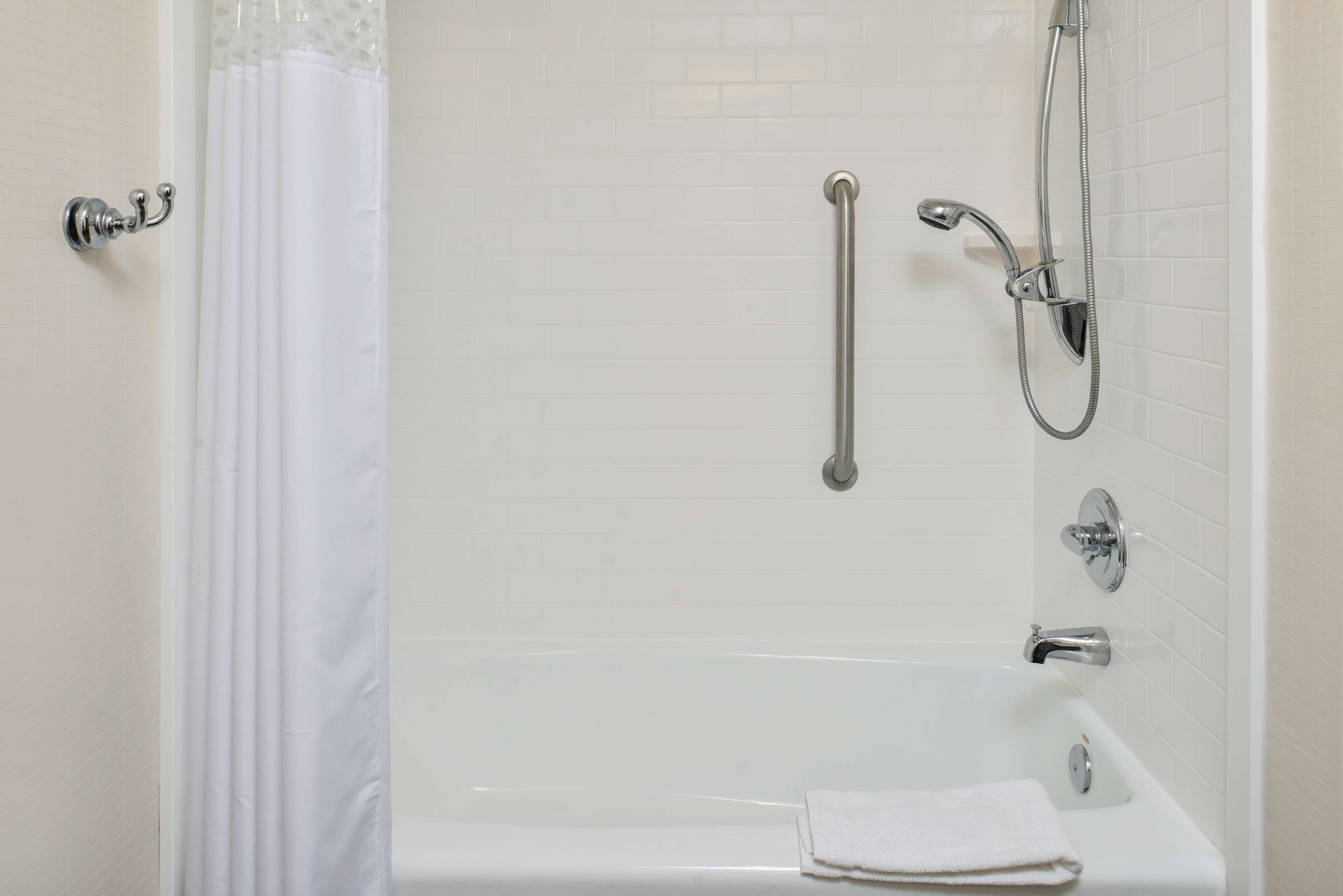 A white bathtub with a handheld showerhead, a grab bar, and a towel on the side.