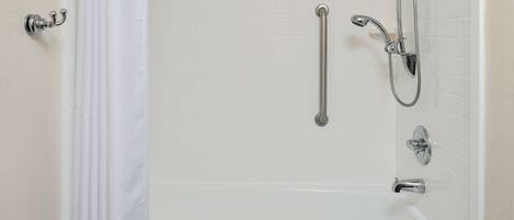 A white bathtub with a handheld showerhead, a grab bar, and a towel on the side.