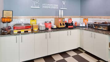 A breakfast buffet area with various food stations, including a coffee station and a fruit display.