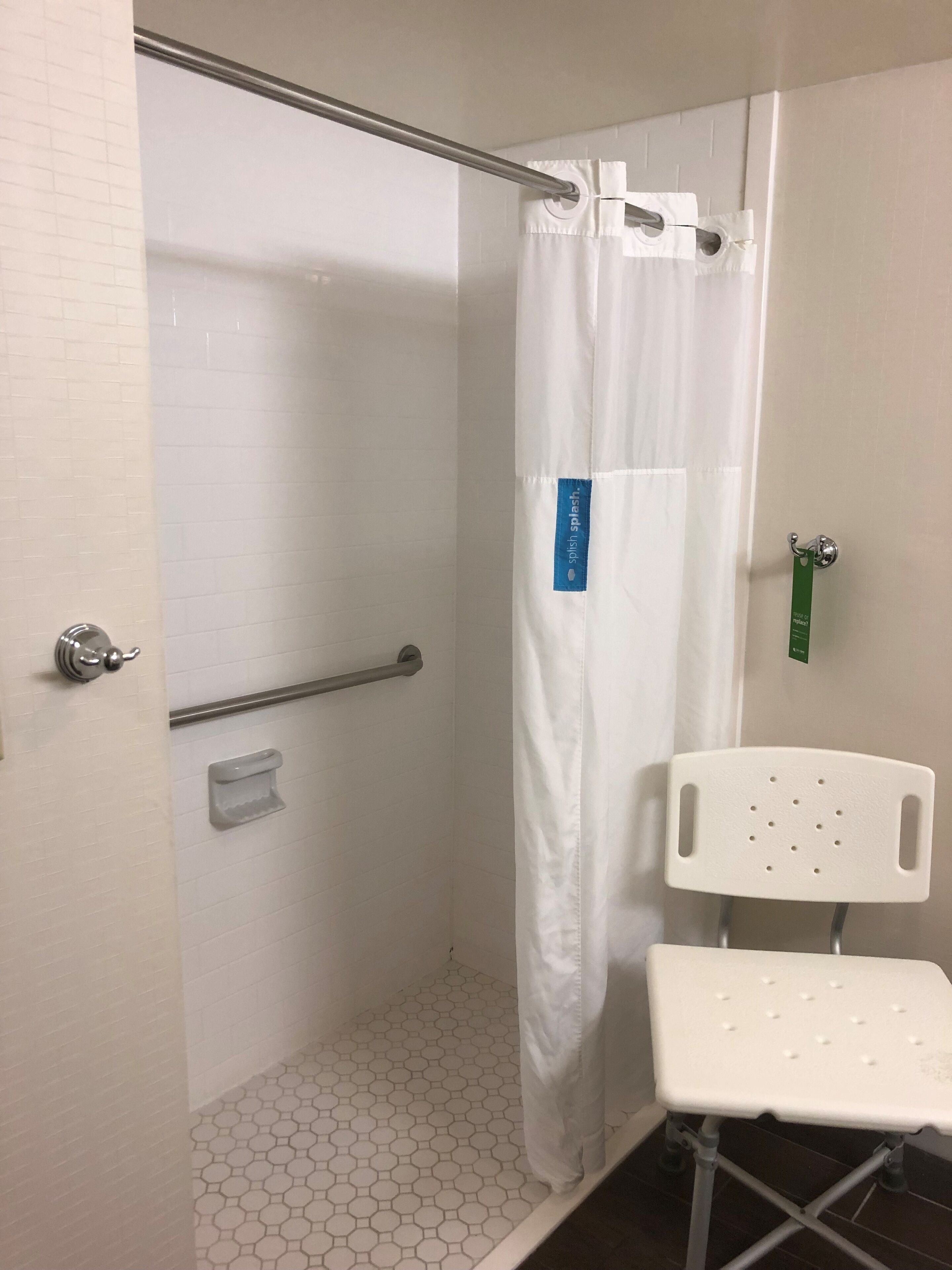 A shower area with a white shower curtain, a grab bar, a white chair, and a small shelf.