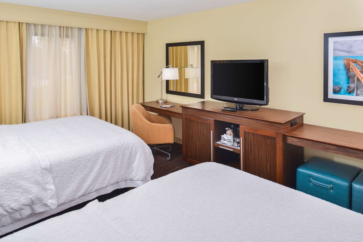 A hotel room with two beds, a desk with a television, a chair, and a small cabinet.