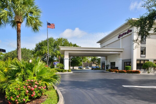 Guests enter under a spacious overhang surrounded by lush greenery and palm trees.