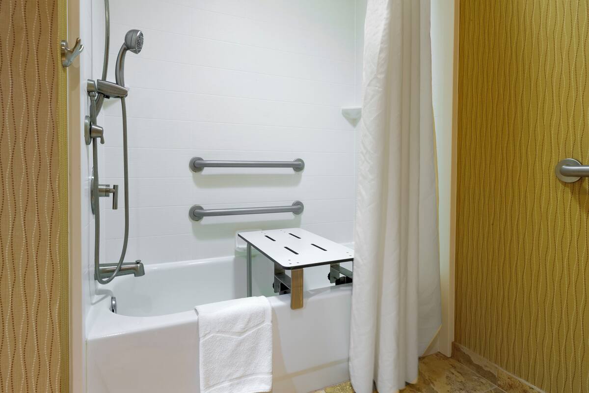 A bathroom with a bathtub, grab bars, a showerhead, and a towel rack.