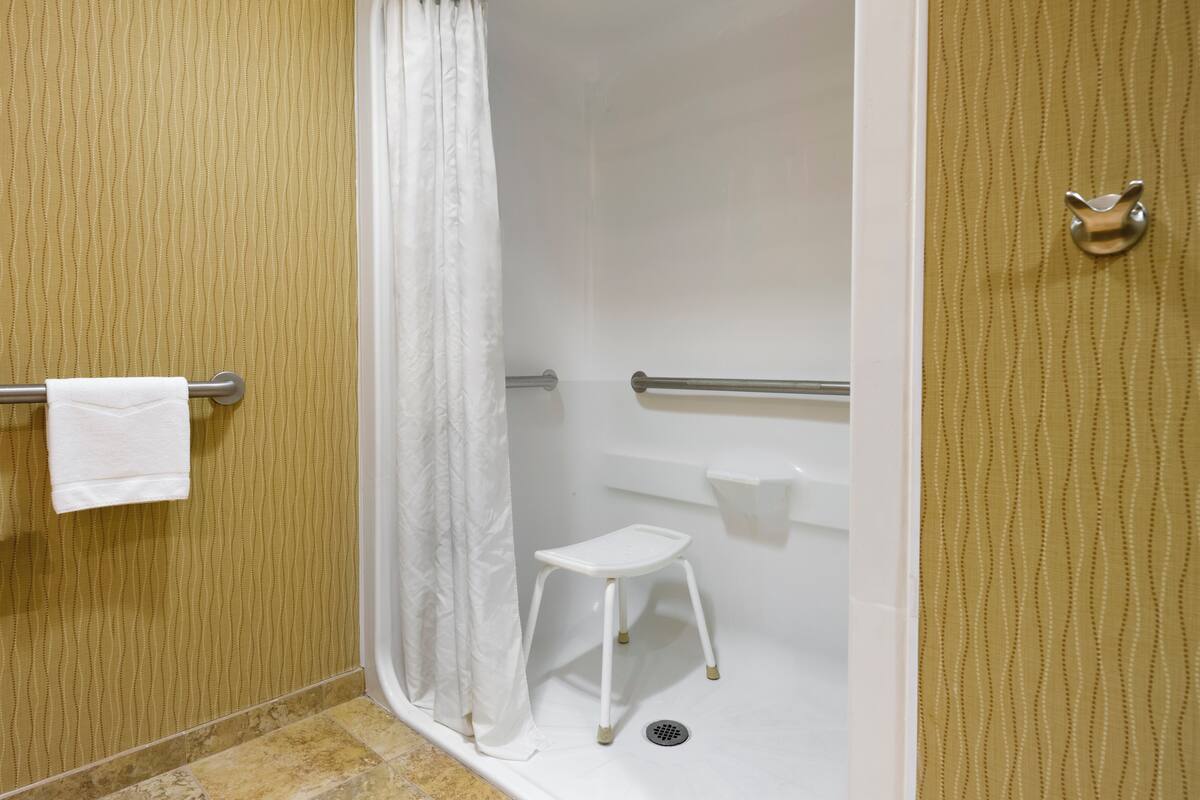 A bathroom with a shower, a white towel on a towel rack, a white step stool, and a door with a cat-shaped handle.