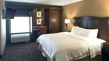 Habitación de hotel con una cama grande, un escritorio, una silla, una lámpara de escritorio, un teléfono y un televisor instalado en la pared.