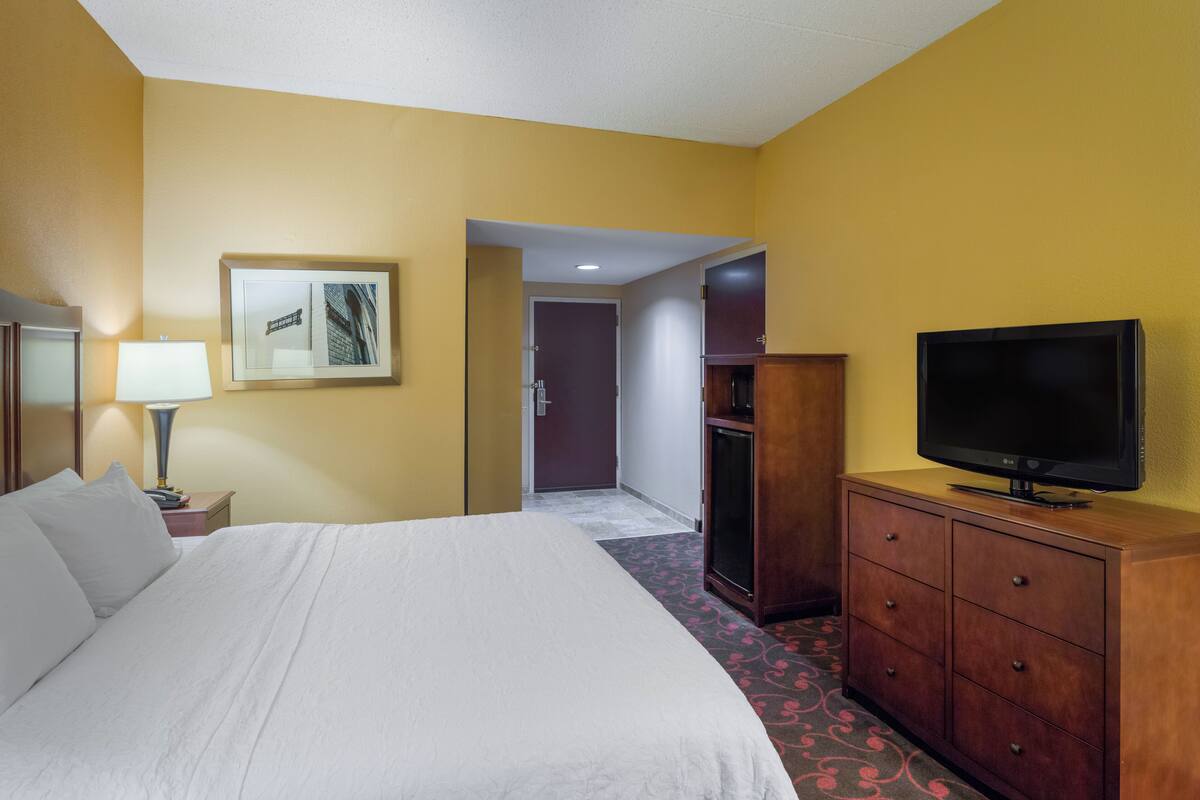 A hotel room with a bed, a television on a wooden cabinet, a lamp, and a framed picture on the wall.