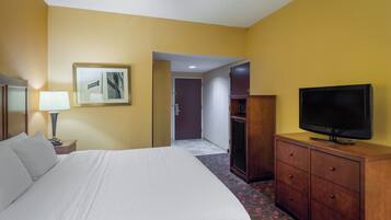Une chambre d’hôtel avec un lit, un téléviseur posé sur une commode en bois, une lampe et un tableau encadré accroché au mur.