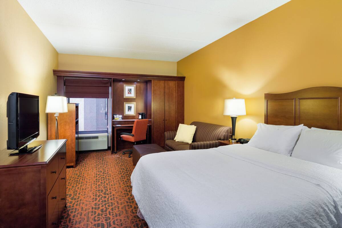 A hotel room with a bed, desk, chair, television, and lamps.