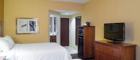 Habitación de hotel con dos camas, un televisor sobre un aparador de madera, un cuadro en la pared y una puerta que da a un baño.