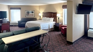 A hotel room with a bed, a desk with a computer, a TV, and a seating area with a bench and chairs. - Hotel Carlisle (Carlisle)