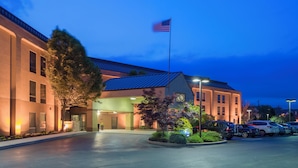 A hotel entrance with a flag, a parking lot, and a building with a blue roof. - Hotel Carlisle (Carlisle)