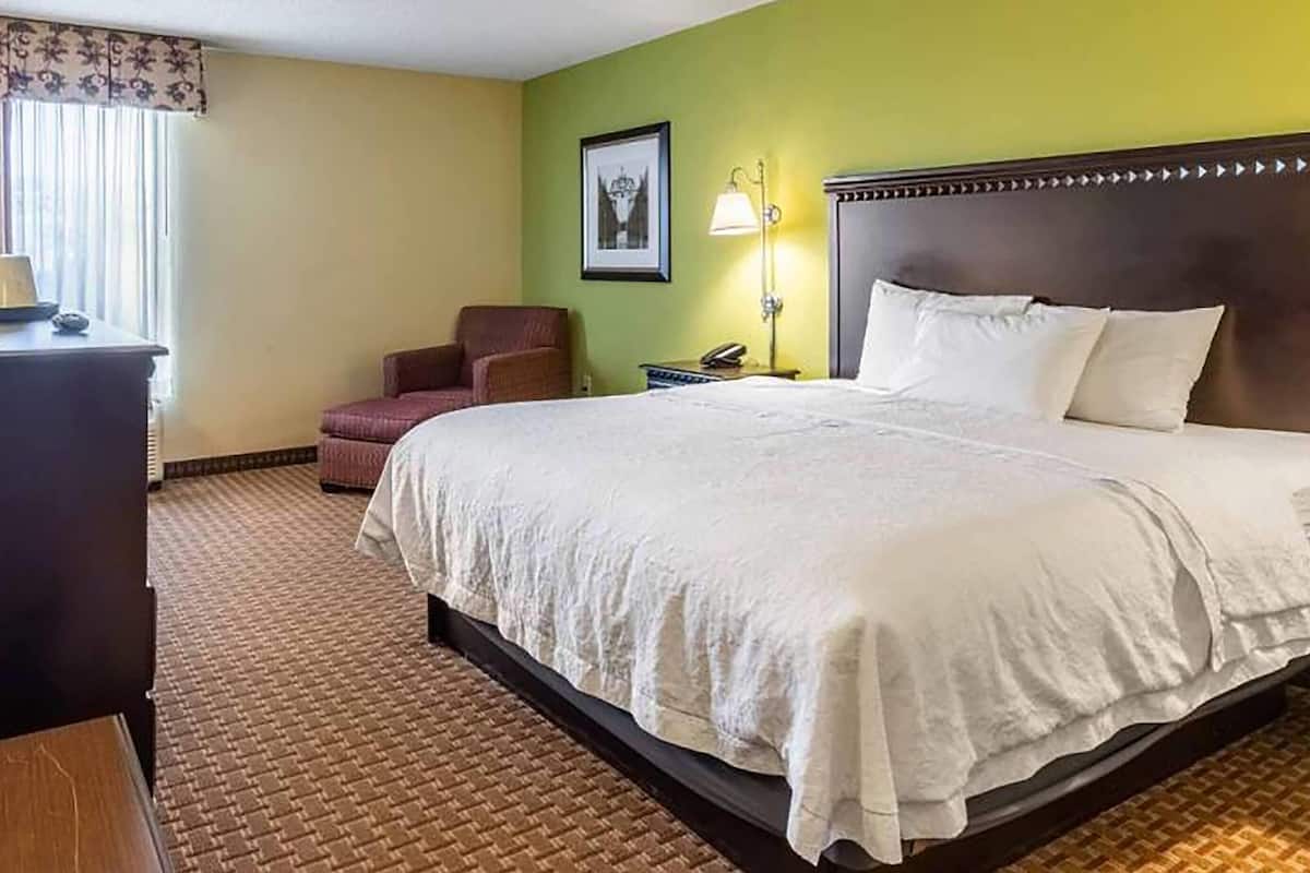 Habitación de hotel con una cama grande, un escritorio, una silla, una lámpara y un cuadro en la pared.