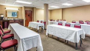 A conference room with multiple tables and chairs, a kitchenette, and a door.