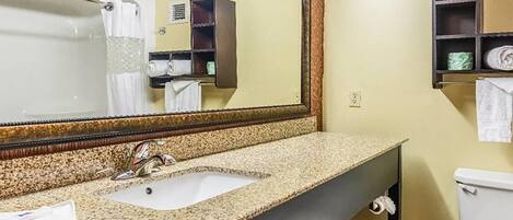 A bathroom with a granite countertop sink, a large mirror, a toilet, and a towel rack.