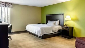 A hotel room with a bed, bedside table, lamp, and a desk with a chair.