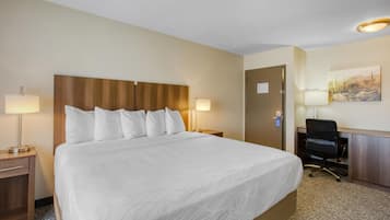 Una habitación de hotel con una cama grande, dos lámparas de noche, un escritorio con una silla y una puerta.