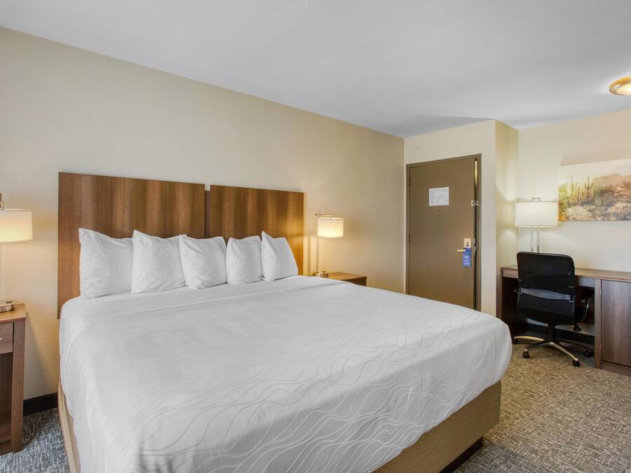 Una habitación de hotel con una cama grande, dos lámparas de noche, un escritorio con una silla y una puerta.