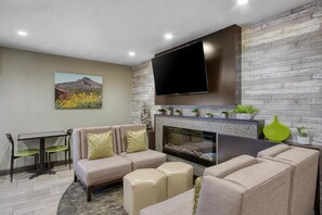 A modern living room with a flat-screen TV mounted on a stone wall, a fireplace, and a dining area with a table and chairs. - Best Western North Phoenix Hotel (Phoenix)