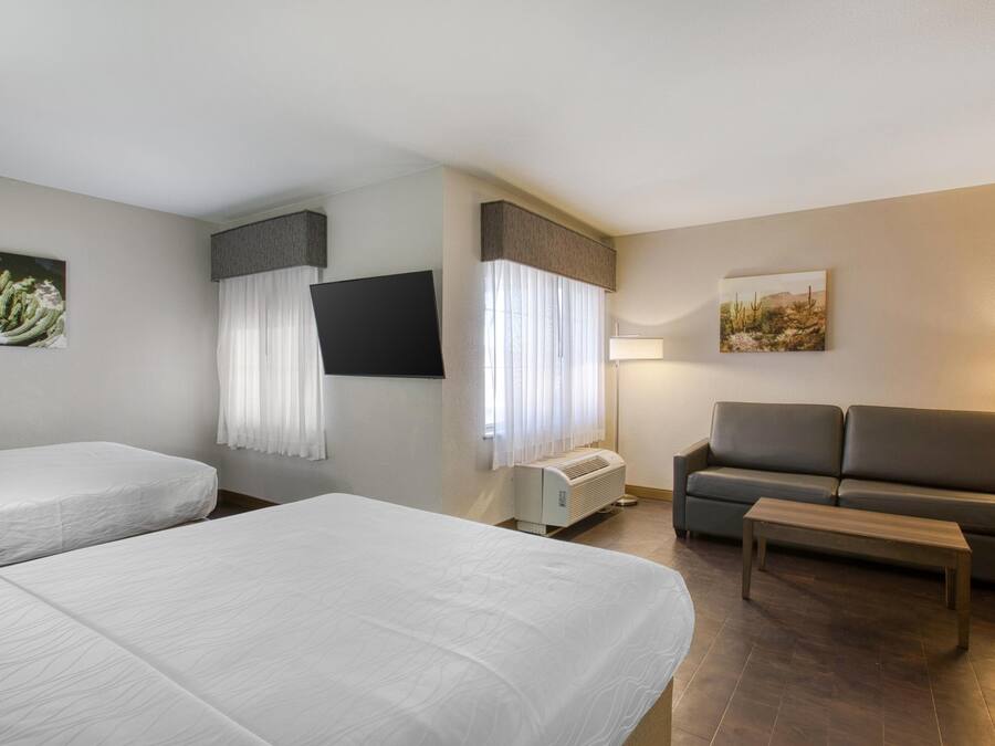 Habitación de hotel con dos camas, un sofá, un televisor y un cuadro en la pared.