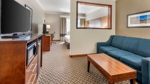 A hotel room with a television, wooden desk, blue sofa, and a large mirror on the wall.