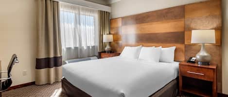 A hotel room with a large bed, a desk, a chair, a lamp, and a window with curtains.