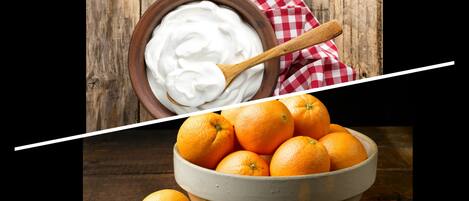 A wooden table with a bowl of oranges and a bowl of white substance, possibly yogurt, with a wooden spoon.