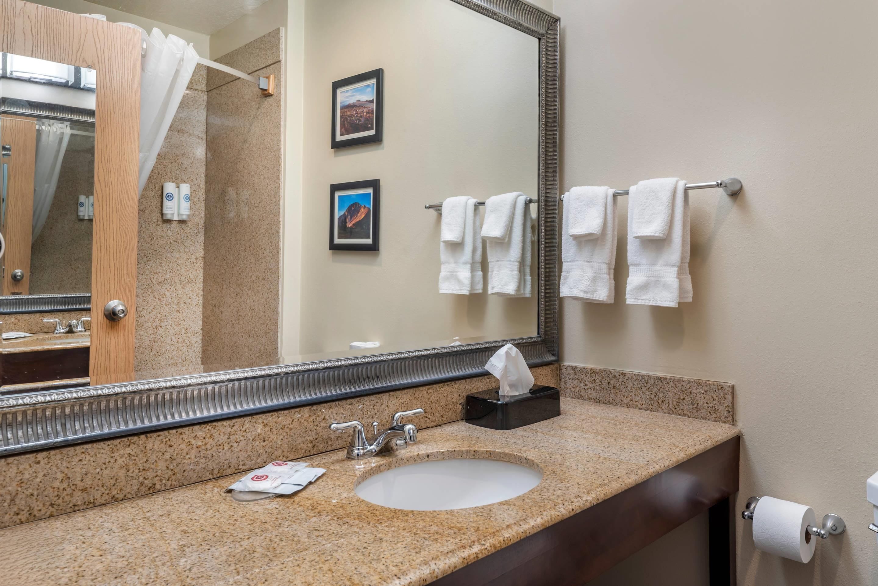 A bathroom with a granite countertop, a sink, a mirror, and a towel rack with white towels.
