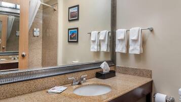 A bathroom with a granite countertop, a sink, a mirror, and a towel rack with white towels.