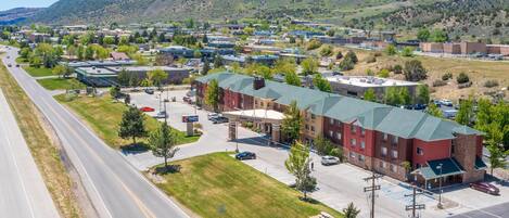 A multi-story hotel with a green roof, parking lot, and a view of a mountainous landscape.