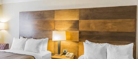 Ein Hotelzimmer mit zwei Betten, einem Holzkopfstück, einer Nachttischlampe, einem Telefon und einem Nachttisch.