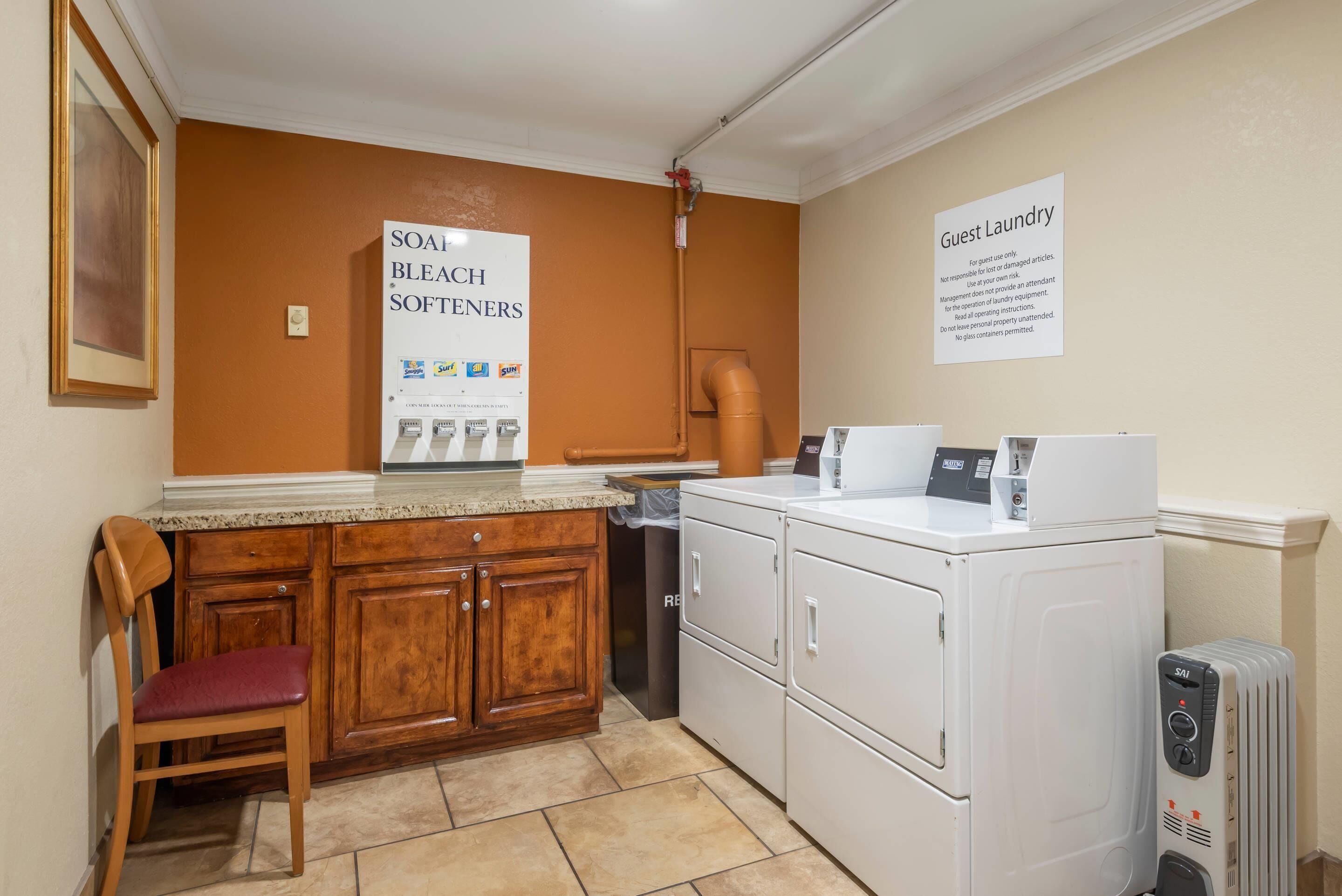 A kitchen with a wooden cabinet, a chair, a white refrigerator, and a sign for guest laundry.