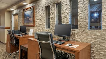 A hotel reception area with a stone wall, two reception desks, black office chairs, and a framed painting.