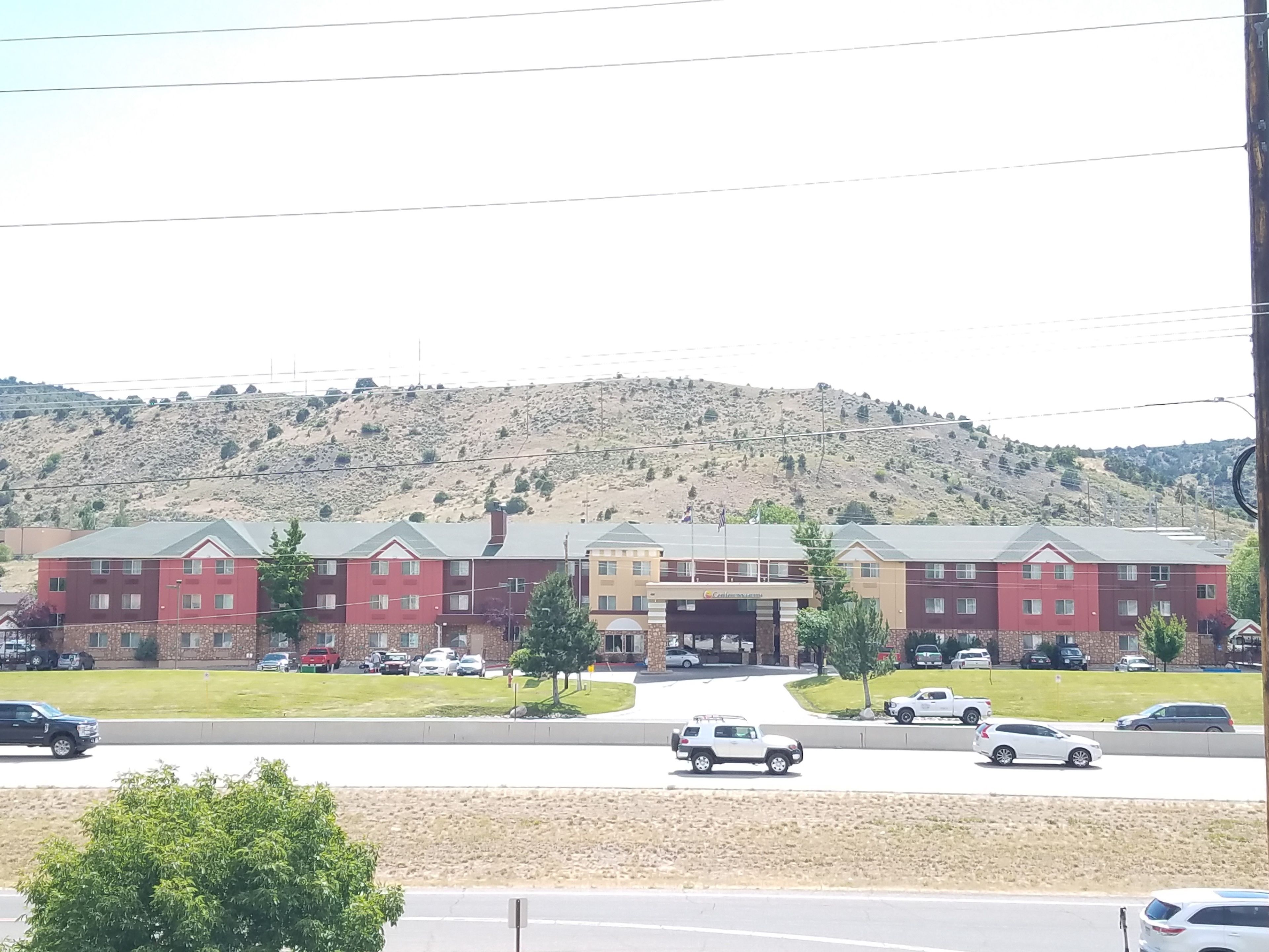 A multi-story building with a central entrance, surrounded by parking lots and a hilly landscape in the background.