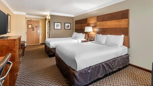 A hotel room with two beds, a desk, a chair, and a TV.